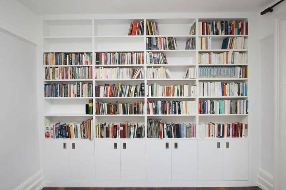 Full view of tall White painted library bookcase with 4-column shelves and bottom closets with steel handles