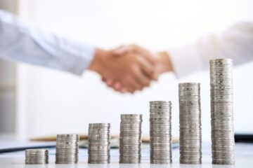 Förderung für Arztpraxen: Handshake vor Münzstapeln als Symbol für finanzielle Unterstützung und Wachstum