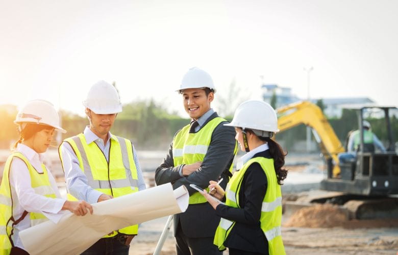 Gruppe von Bauingenieuren und Projektleitern mit Bauhelmen und Bauplänen auf einer Baustelle – Baufinanzierung für Ärzte mit professioneller Unterstützung.