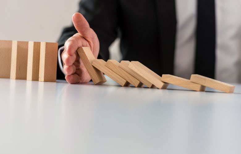 Hand stoppt fallende Dominosteine, symbolisiert Schutz vor Risiken durch eine Praxisausfallversicherung.