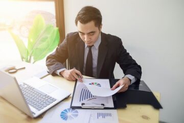 Geschäftsanalyst in Anzug analysiert Diagramme und Verkaufsberichte für den Praxisverkauf an Investoren.