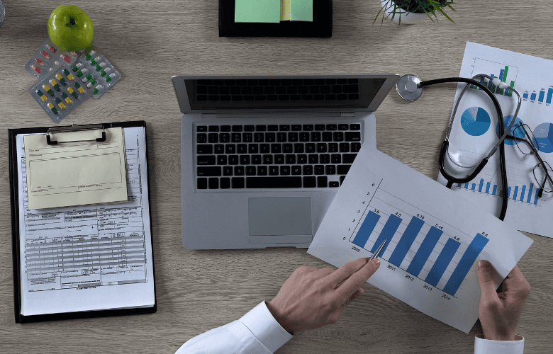 Schreibtisch mit Laptop, Diagrammen und Stethoskop – Symbol für datengetriebenes Online-Marketing in Arztpraxen.