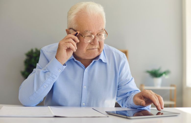 Älterer Arzt im Ruhestand recherchiert Jobmöglichkeiten und flexible Arbeitsmodelle auf einem Tablet.