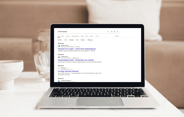 Laptop auf einem Tisch mit geöffnetem Browser, der Google-Suchergebnisse mit SEA-Anzeigen für Ultraschallgeräte anzeigt.