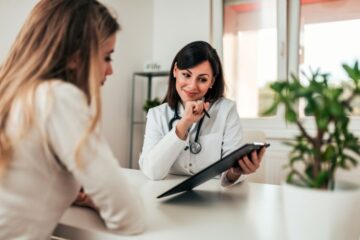 Patientin während der Patientenaufklärung mit Ärztin, die einen Aufklärungsbogen erklärt