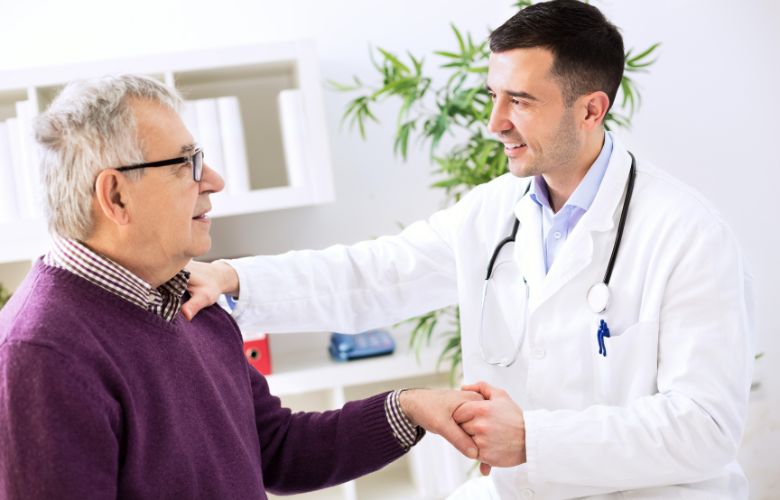 Arzt hält die Hand eines älteren Patienten und lächelt – Fokus auf Patientenzufriedenheit und persönliche Betreuung.