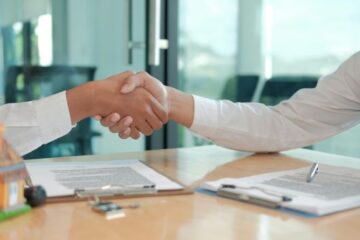 Händedruck über einem Schreibtisch mit Verträgen und Schlüsseln zum Abschluss eines Mietvertrags für eine Arztpraxis.