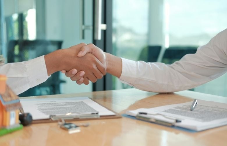 Händedruck über einem Schreibtisch mit Verträgen und Schlüsseln zum Abschluss eines Mietvertrags für eine Arztpraxis.