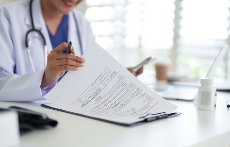 Dokumentationspflicht Arzt Ärztin im Kittel prüft medizinische Unterlagen auf einem Klemmbrett; Fokus auf Hand mit Stift und Dokument.