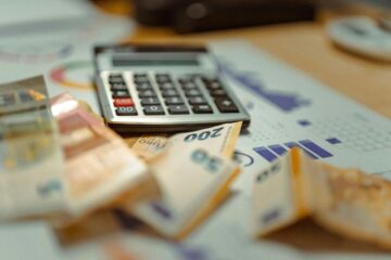 Euro-Banknoten und ein Taschenrechner auf Finanzgrafiken zur steuerlichen Planung einer Praxisgründung.