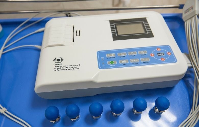 Ein gebrauchtes EKG-Gerät mit Tastenfeld und sechs blauen Saugelektroden auf einer blauen Arbeitsfläche.