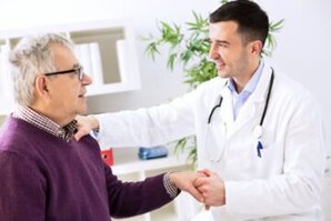 Arzt hält die Hand eines älteren Patienten und lächelt – Fokus auf Patientenzufriedenheit und persönliche Betreuung.