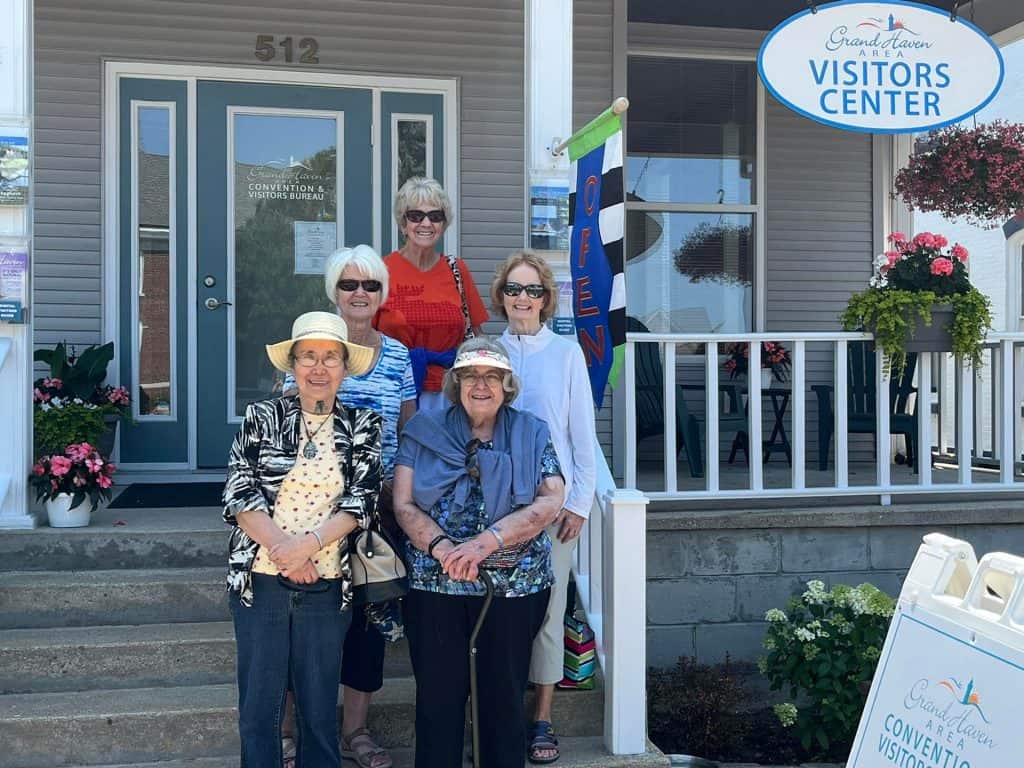 Group of women standing outside Grand Haven Visitors Center in daytime.