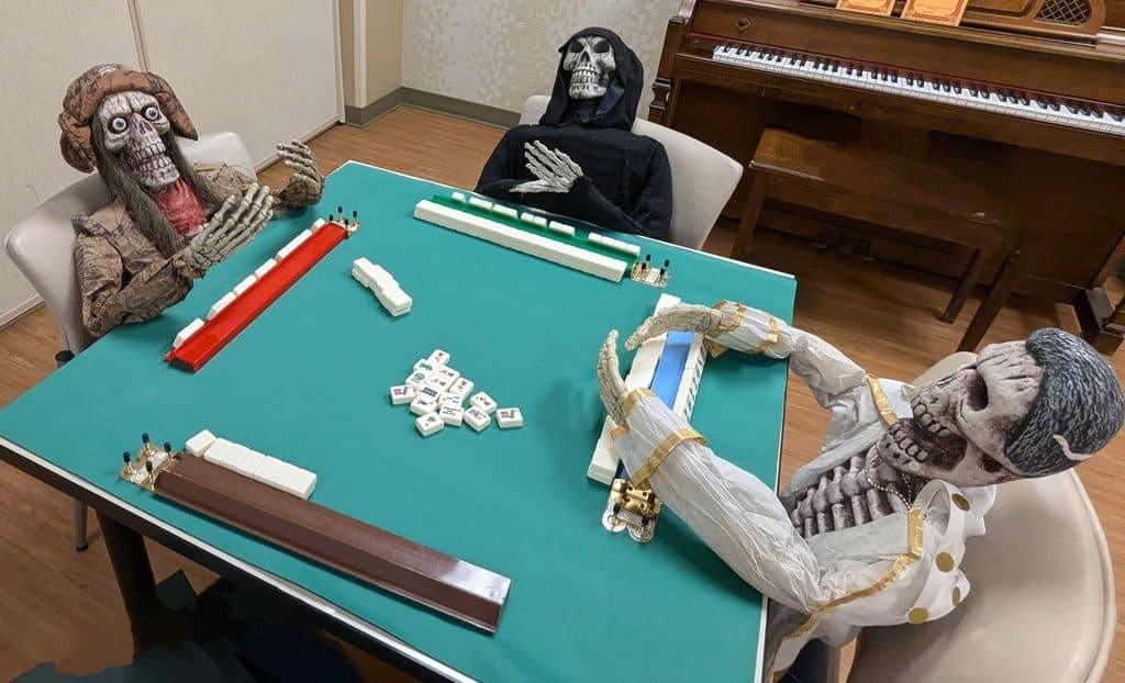 Humorous skeletons playing Mahjong game at table for Halloween decor.