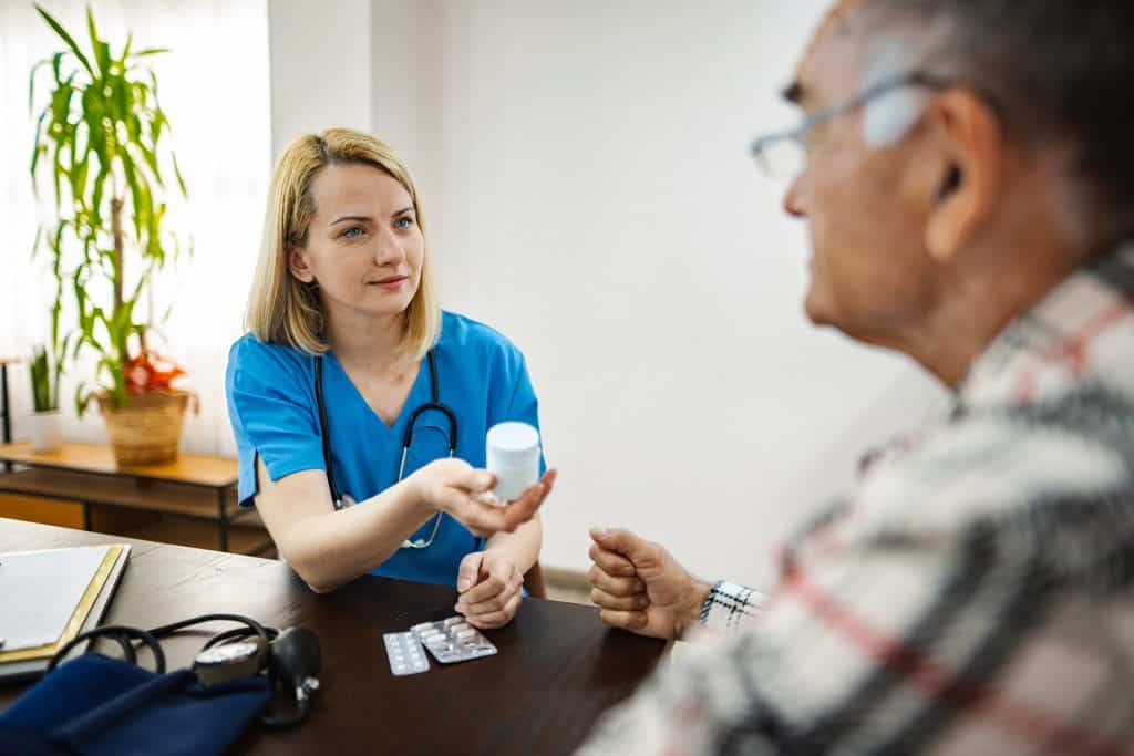 Nurse providing medication guidance to senior patient in a healthcare setting.