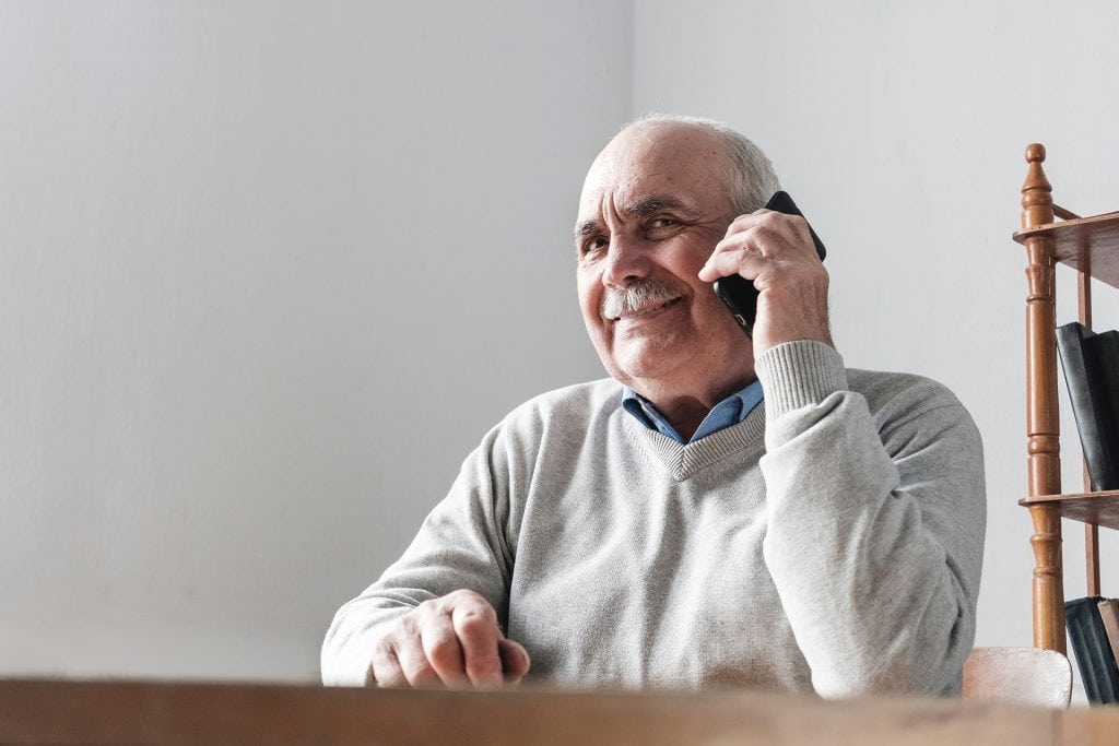 Elderly man talking on phone, smiling, in a volunteer-related setting.