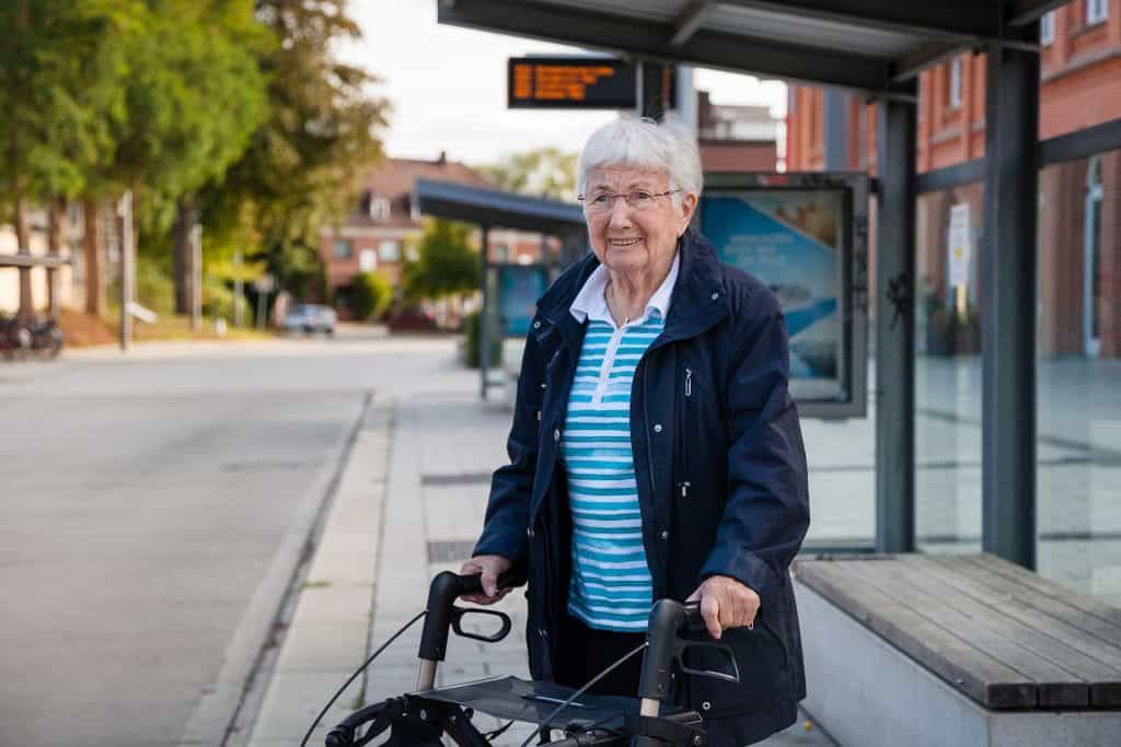 Senior woman with walker waiting at bus stop in urban area.