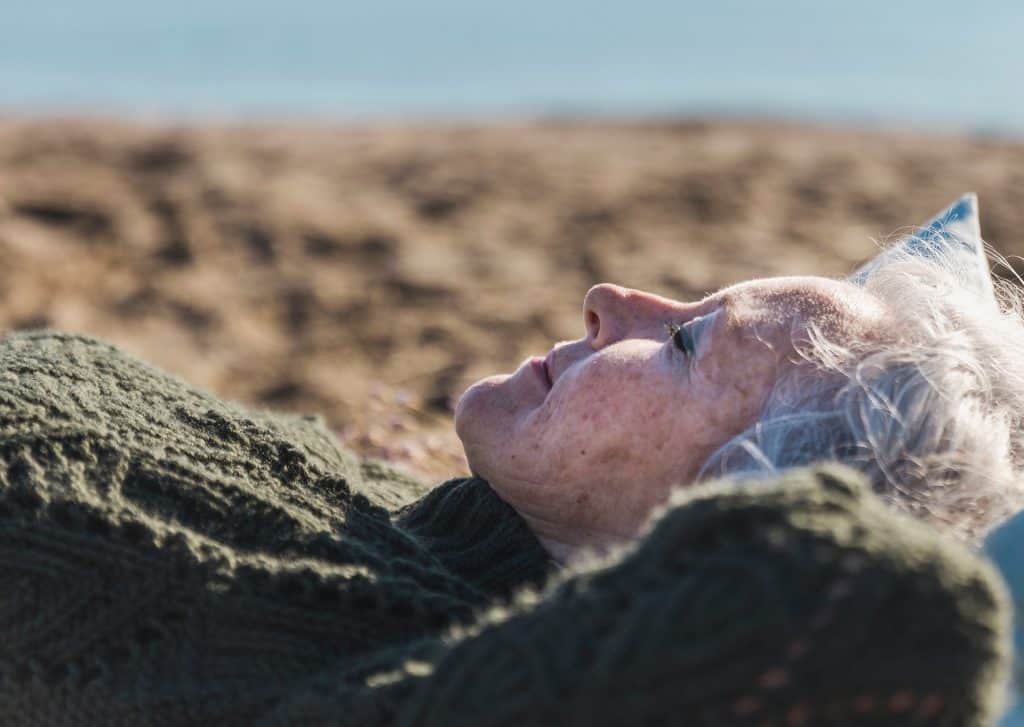 Elderly woman lying on the beach, practicing mindfulness and relaxation.