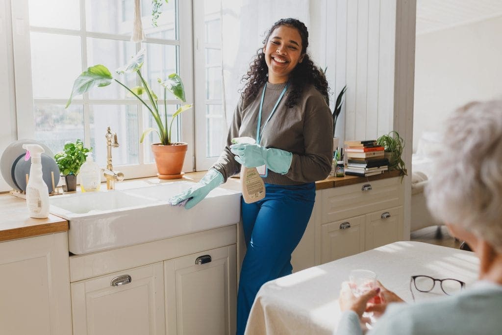 Caregiver providing in-home support services to elderly woman in kitchen.