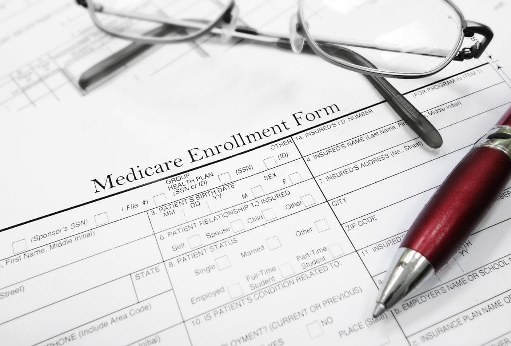 Medicare enrollment form with glasses and pen on desk.
