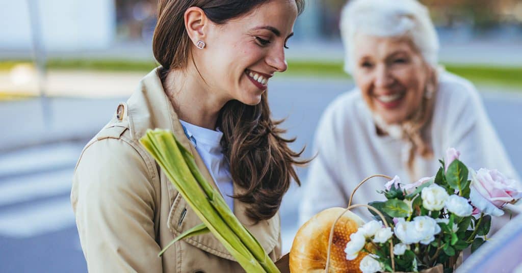 Woman receiving flowers from senior woman outdoors, smiling happily.