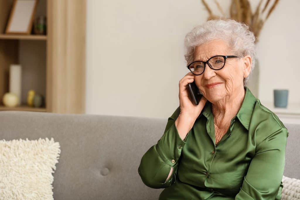 Elderly woman with glasses talking on mobile phone at home.