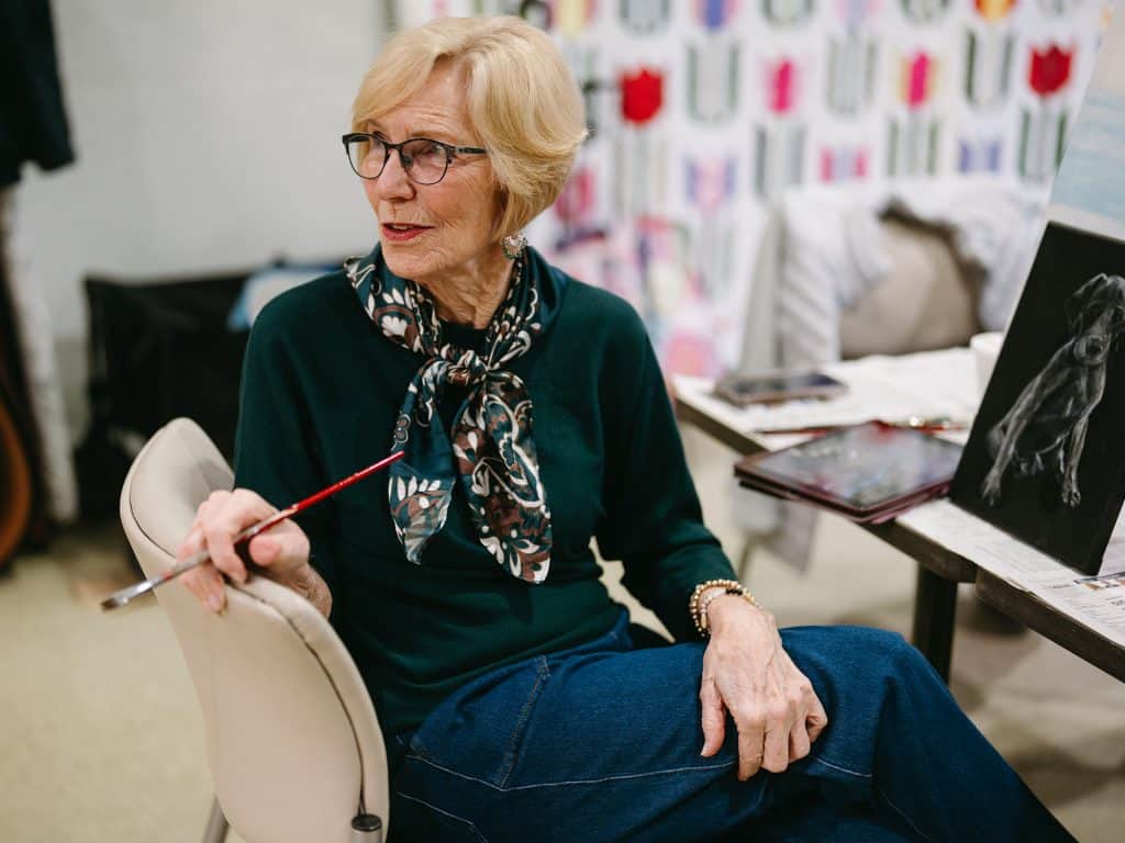 Elderly woman painting with a brush in an art studio.