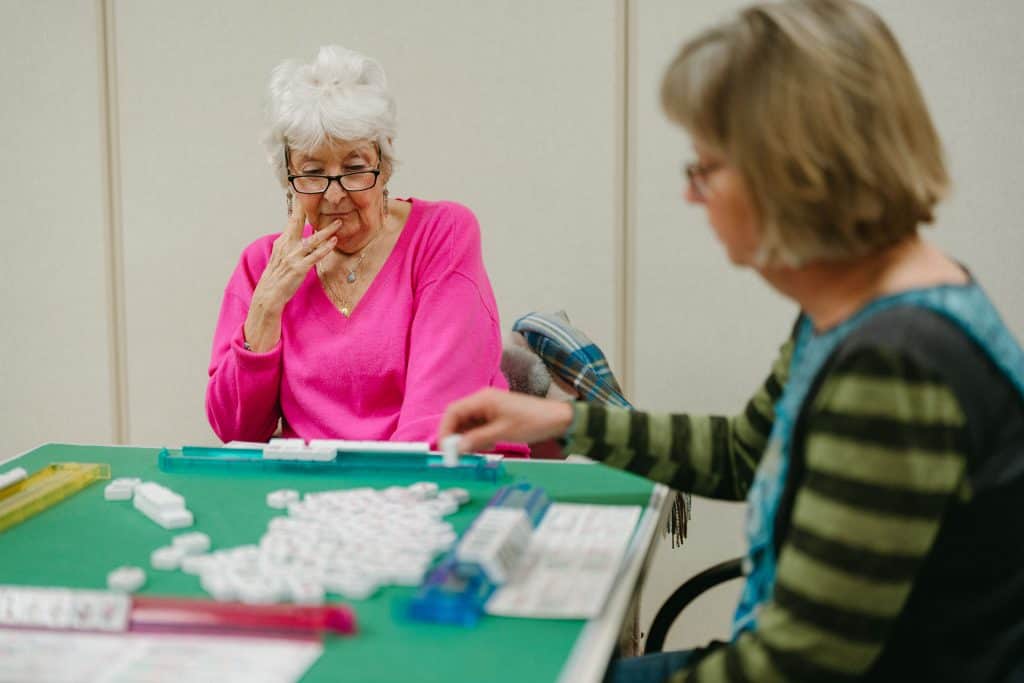 Two senior women playing Rummikub at a table, enjoying a game together.