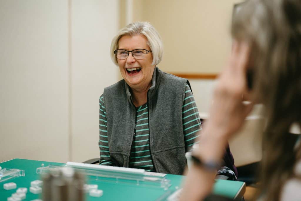 Elderly woman enjoying a game of Mahjong with friends.
