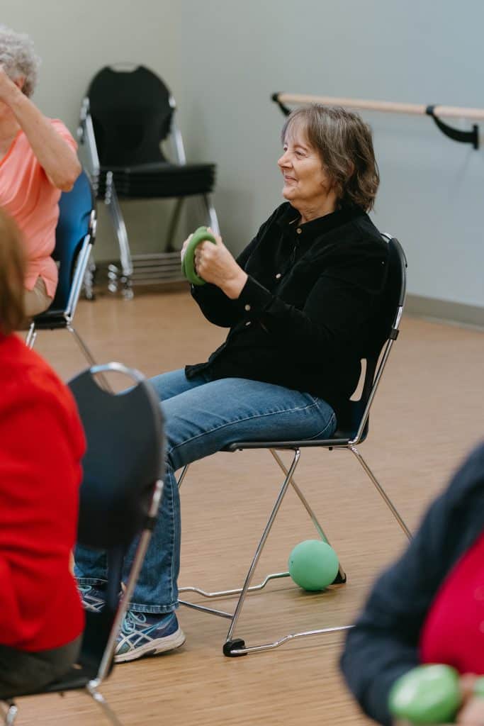 Older woman exercising with green weights in senior fitness class.