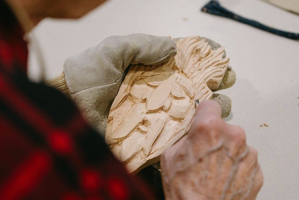 Close-up of person carving wood with a chisel and gloves.