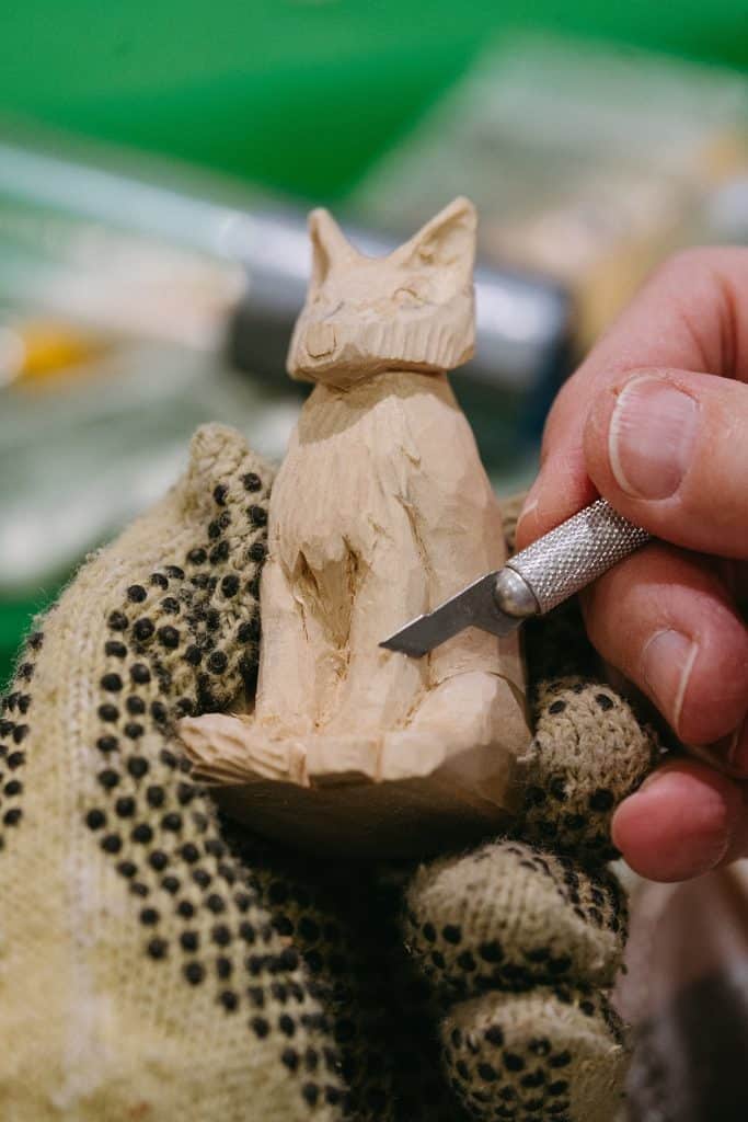 Hand carving a wooden cat sculpture with a craft knife.
