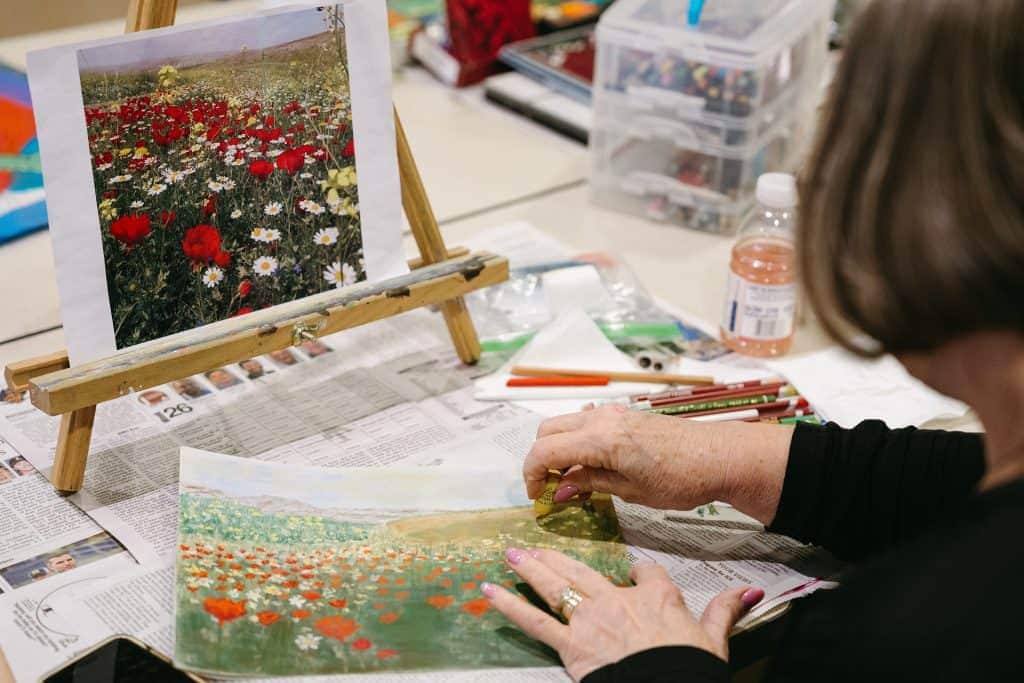 Person painting a colorful flower field on paper at a workspace.