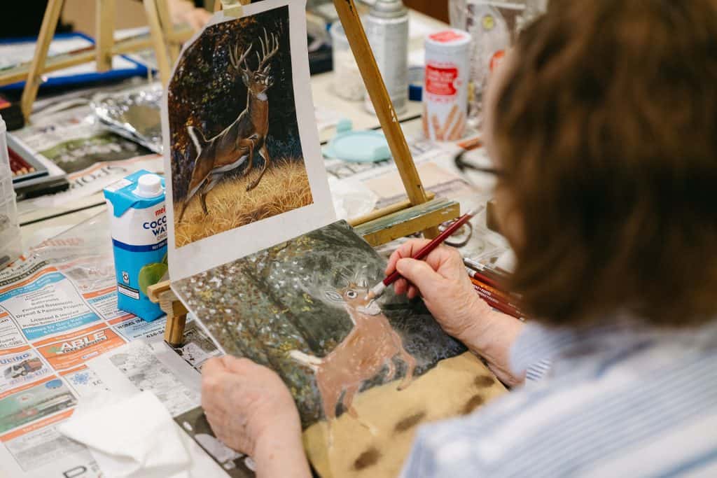 Artist creating detailed wildlife painting of a deer in a forest setting.