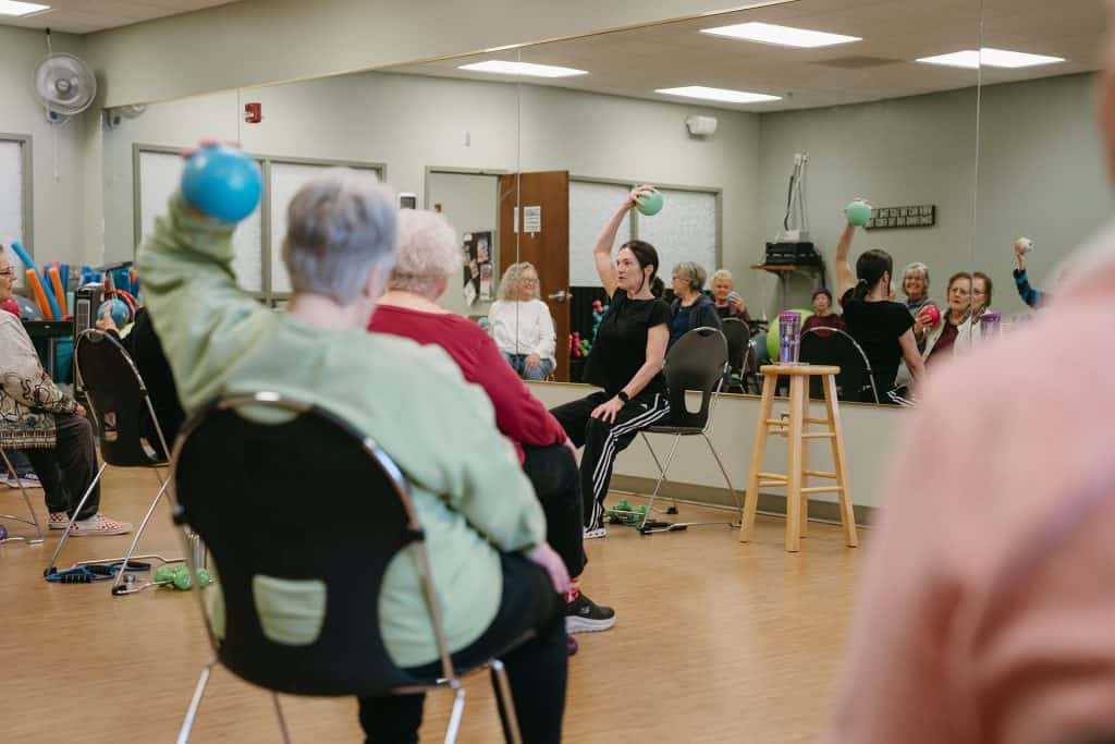 Elderly seniors participating in a fitness class with light weights in a community center.