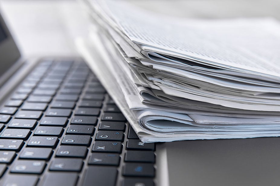 Pila di giornali e documenti su tastiera di laptop, simbolo della sezione Press & Media e della comunicazione aziendale Nepta.