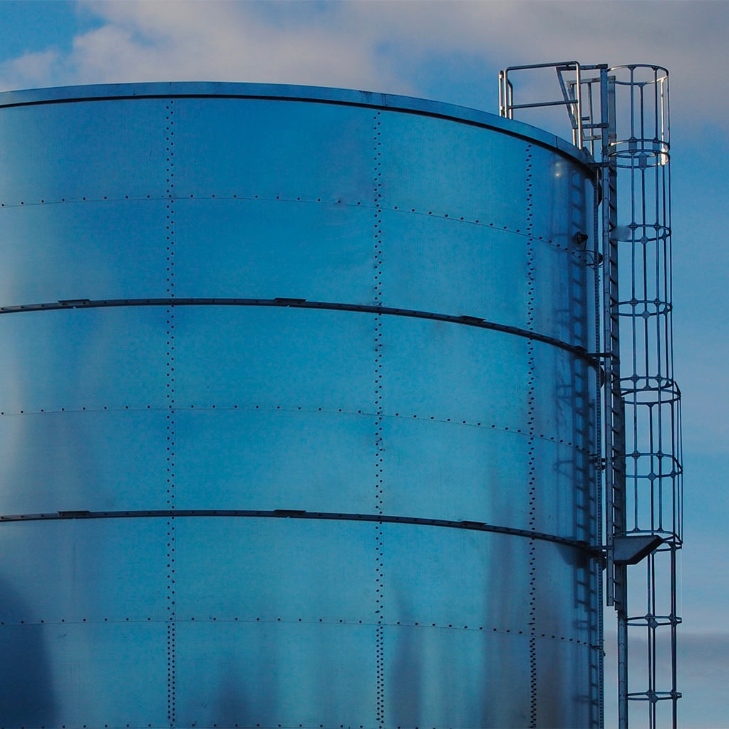 Immagine in primo piano di un grande serbatoio idrico cilindrico in metallo lucido con una scala di sicurezza. Il serbatoio simboleggia le fasi di adduzione e distribuzione dell'acqua potabile e l'impegno di Nepta/Italgas nel garantire un approvvigionamento continuo e nel minimizzare le dispersioni della rete idrica.