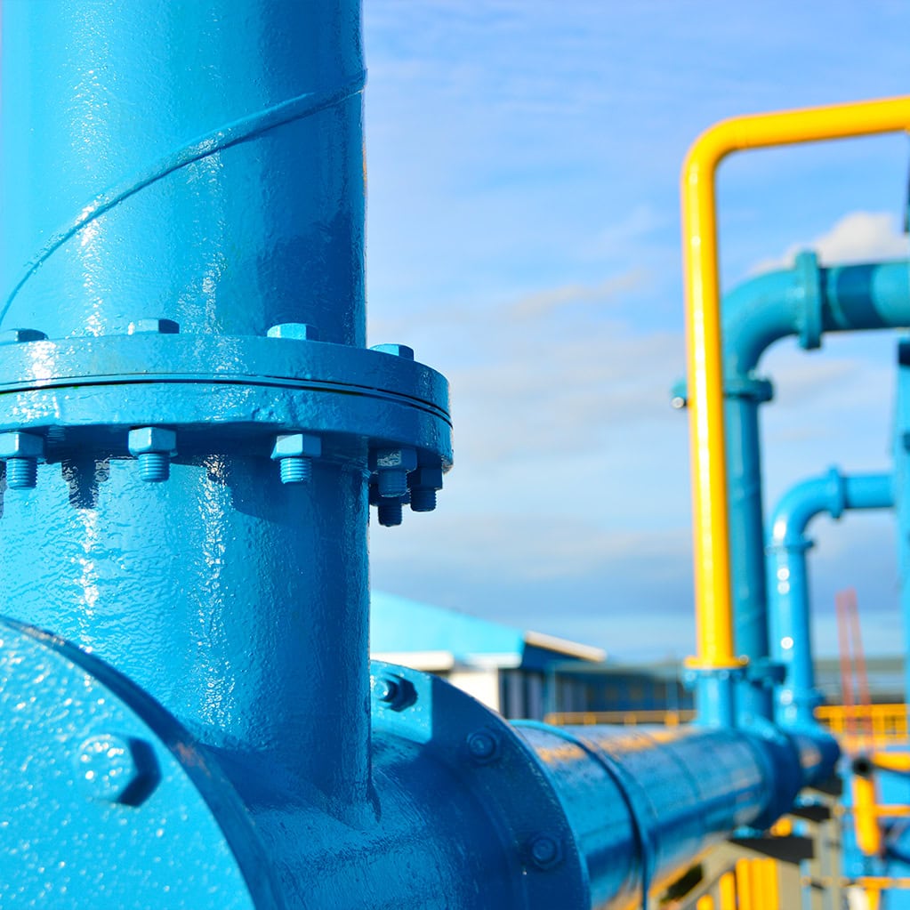 Primo piano ravvicinato di un complesso sistema di tubazioni industriali e flange in metallo verniciato di blu brillante, con dettagli gialli. L'immagine simboleggia la vasta rete di distribuzione idrica del Gruppo Nepta/Italgas, che garantisce la continuità del servizio e la sicurezza dell'acqua a case e industrie.