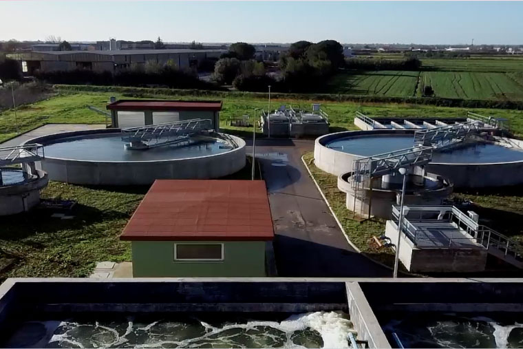 Veduta aerea di un impianto di potabilizzazione dell'acqua, con grandi vasche di trattamento circondate da campi, che rappresenta l'infrastruttura di Acqualatina S.p.A. nel Lazio Meridionale.