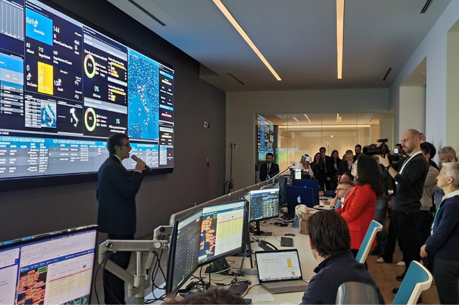People observe a presentation in a control room with large screens displaying data and maps related to Italgas operations.