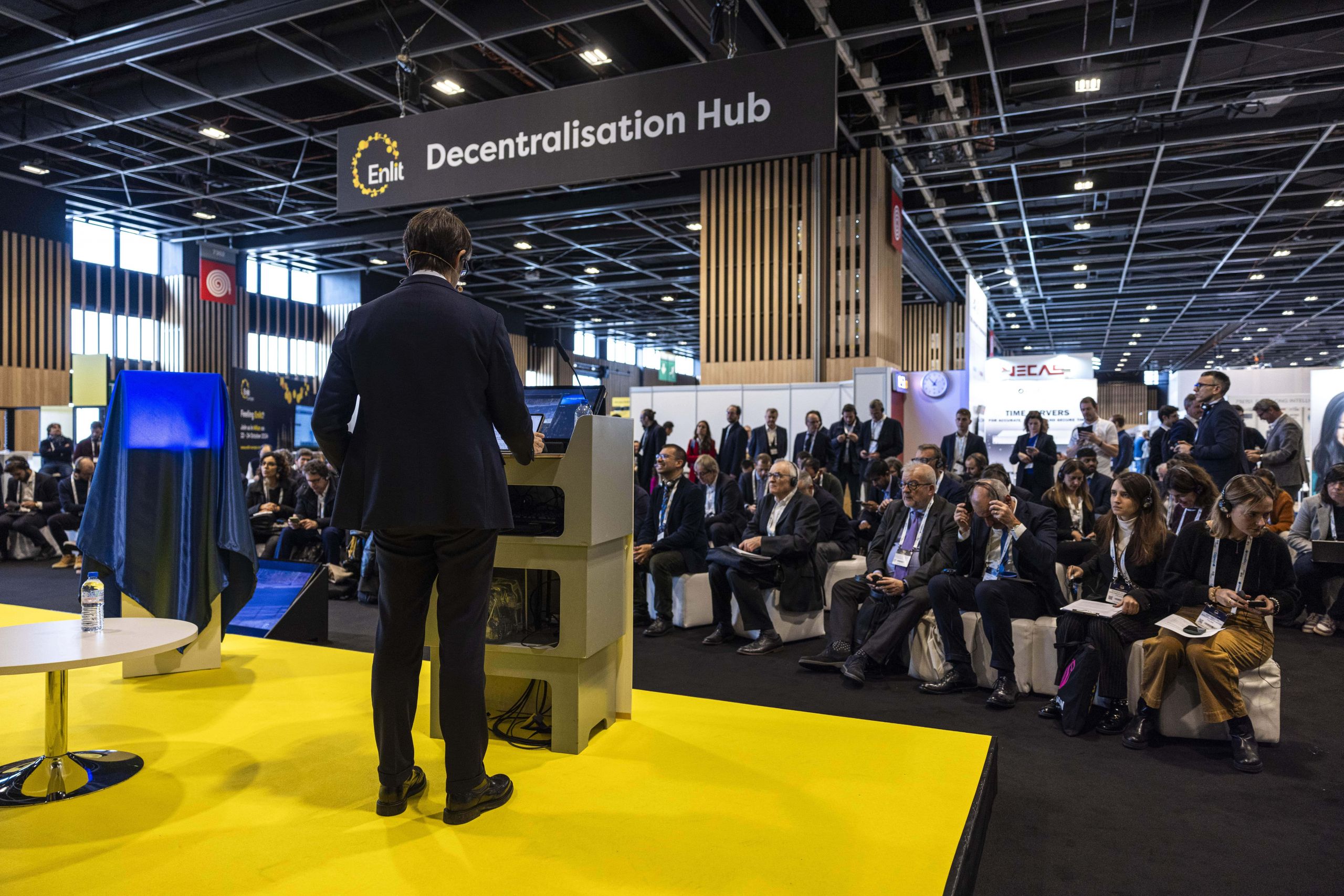 A speaker presents at the "Decentralisation Hub" of an Enlit event. The audience, seated and attentive, consists of professionals and attendees.