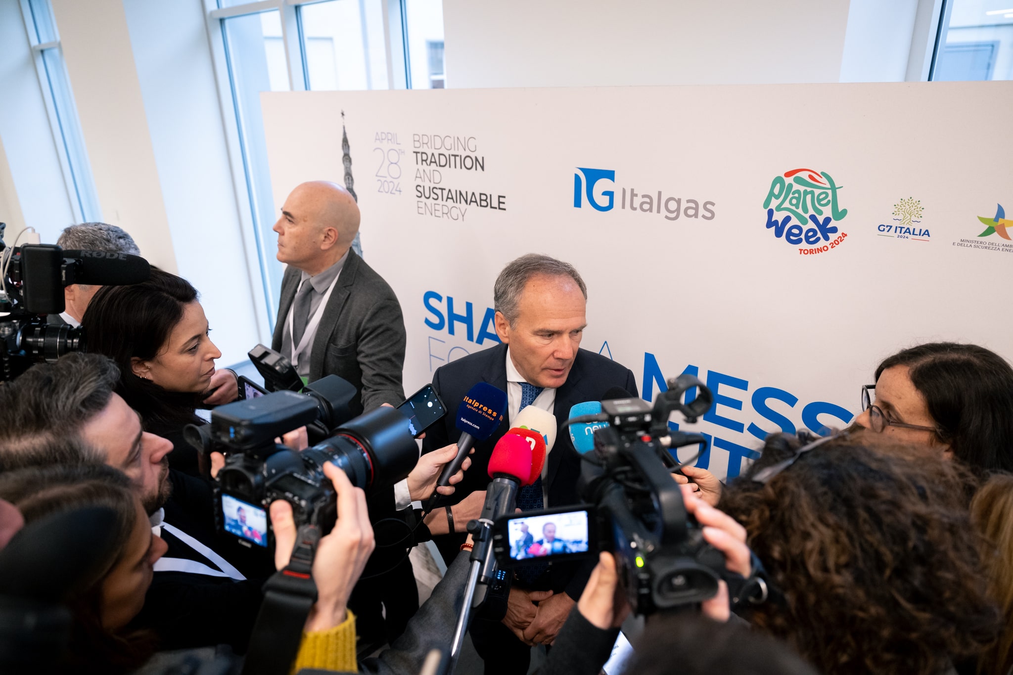 Man addresses media at Planet Week event by Italgas with microphones and cameras pointed at him.