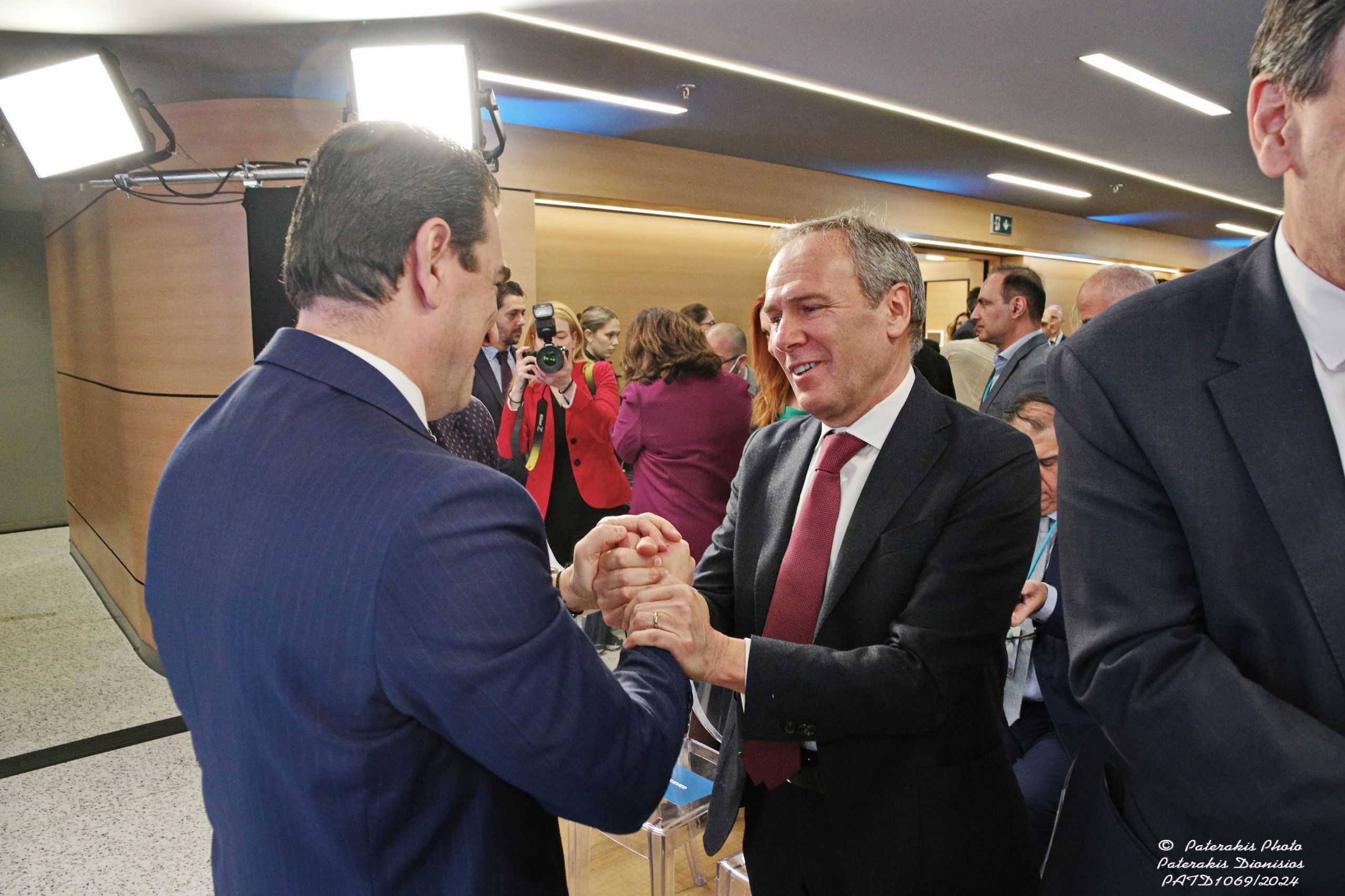 Paolo Gallo and another man in suits shaking hands with smiles, others in background, indoor event setting.