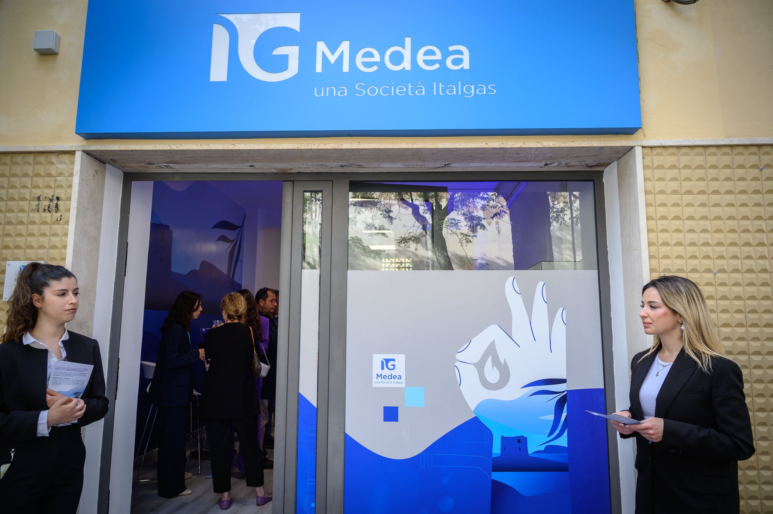 Entrance to Medea Italgas infopoint with people, blue signage, and logo.