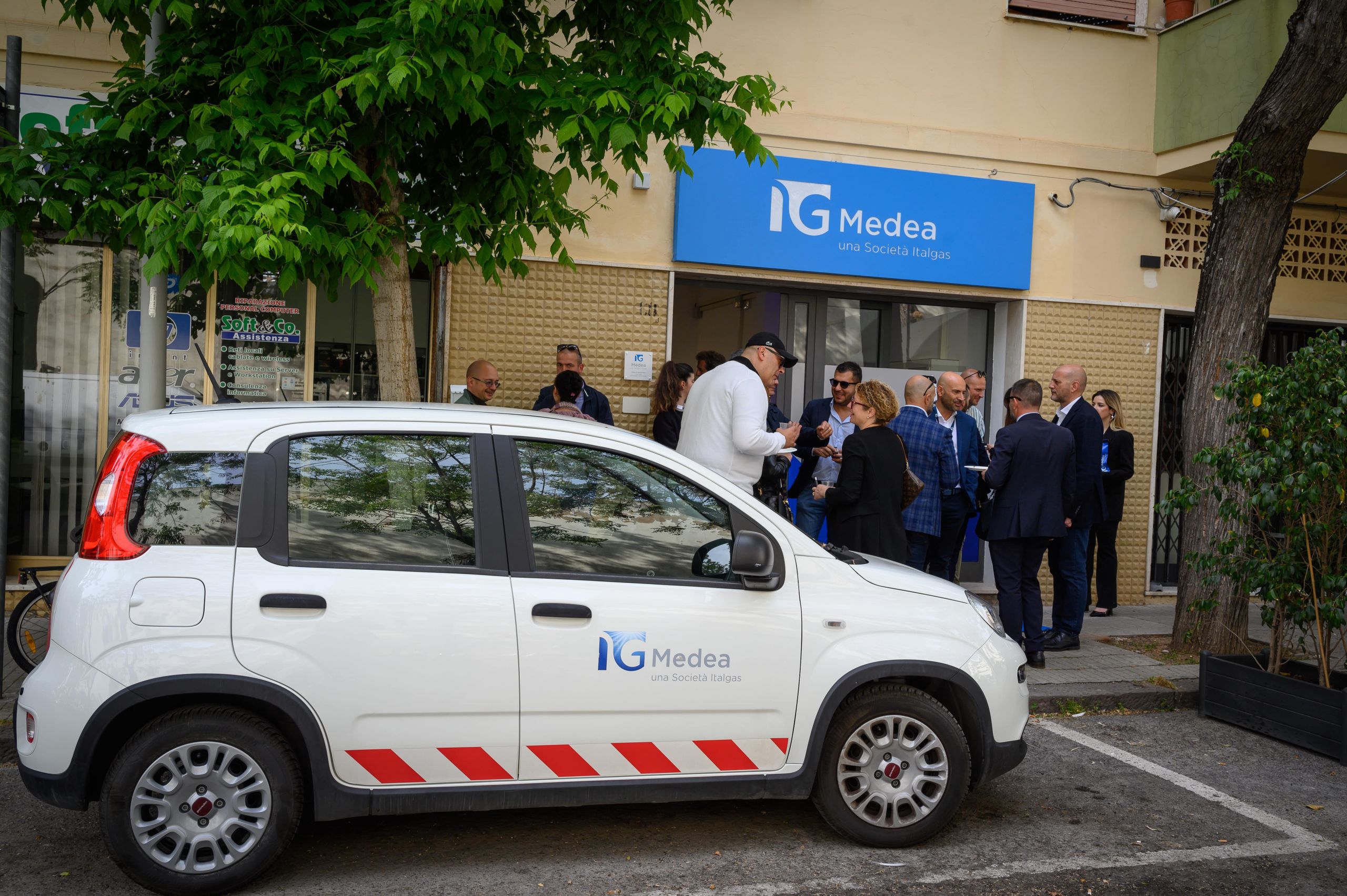 People gather outside Medea Italgas infopoint next to a branded car.