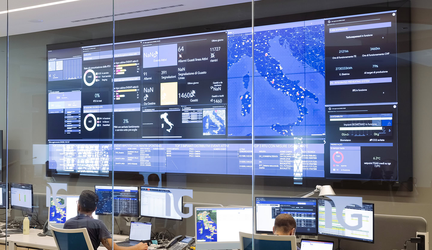 Italgas control room with people at the PC, large monitors showing data for energy efficiency and emissions reduction.
