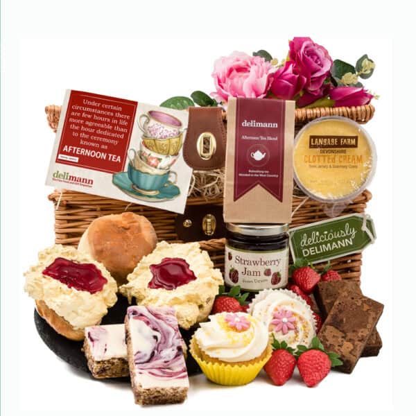 A hamper brimming over with various delights, including scones, clotted cream, tea, jam, cupcakes, brownies.