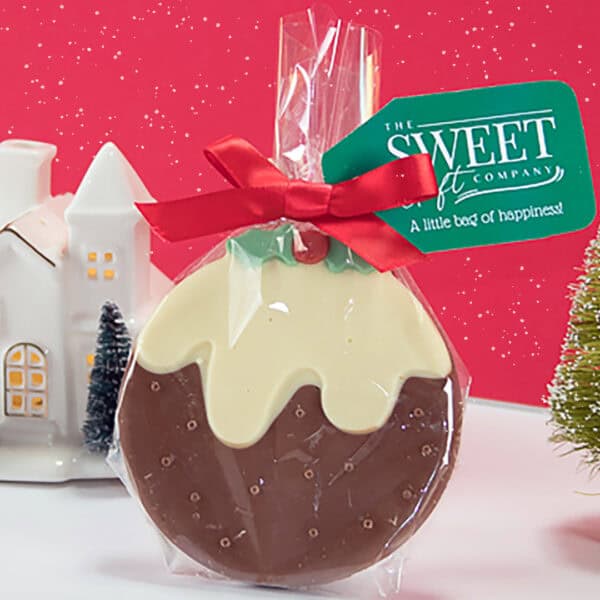 A Belgian Chocolate Christmas Pudding treat, wrapped in clear plastic with a red ribbon and a tag that reads "The Sweet Company: A little bag of happiness!" against a red festive background.