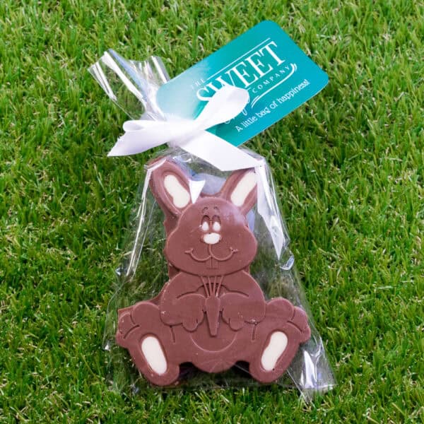 A delightful Milk & White Chocolate Bunny in clear packaging with a vibrant green label is nestled on lush grass.