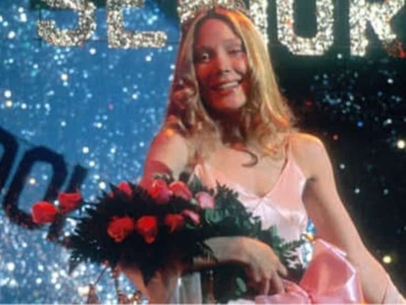 A young woman in a pink dress holds a bouquet of roses on stage, smiling, with sparkling “SENIOR” letters in the background—perfect for 31 Days of Horror inspiration.